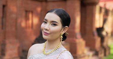 Portrait of Thai woman in traditional costume looking at camera and smiling in ancient temple. video