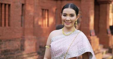 retrato de mujer tailandesa saludo de respeto en traje tradicional de tailandia. mujer joven mirando a la cámara y sonriendo en el antiguo templo. video