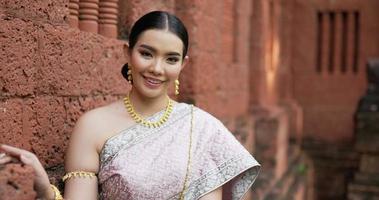 Portrait of Thai woman salute of respect in traditional costume of thailand. Young female looking at camera and smiling in ancient temple.