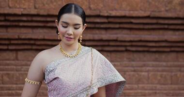 retrato de mujer tailandesa saludo de respeto en traje tradicional de tailandia. mujer joven mirando a la cámara y sonriendo en el antiguo templo. video