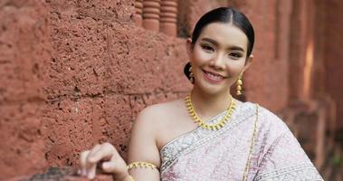 Porträt einer thailändischen Frau in traditioneller Tracht, die in die Kamera schaut und im alten Tempel lächelt. video