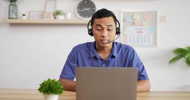 porträt eines jungen asiatischen kundendienst-support-agenten telemarketer mit headset, der einen laptop anschaut, führt einen internet-videoanruf für eine geschäftskonferenz. video