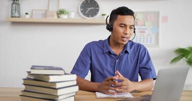 Portrait of Young Asian customer service support agent telemarketer wearing headset looking at laptop make business conference internet video call.