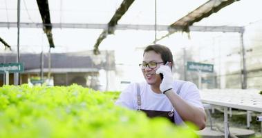 joven agricultor asiático hablando por teléfono móvil mientras revisa el roble verde fresco con feliz