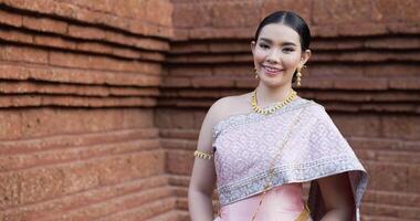 porträtt av thailändsk kvinna salut av respekt i traditionell kostym av thailand. ung kvinna tittar på kameran och ler i antika tempel. video