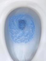 Top view of toilet bowl, blue detergent flushing in it photo