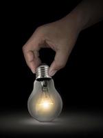 Hand holding glowing light bulb on dark background photo