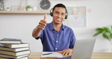 Portrait of Young Asian customer service support agent telemarketer wearing headset showing thumb up make business conference internet video call.