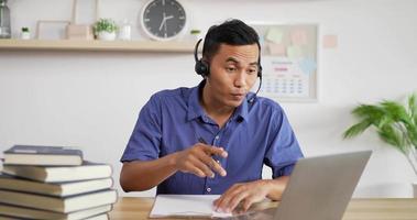 porträt eines jungen asiatischen kundendienst-support-agenten telemarketer mit headset, der einen laptop anschaut, führt einen internet-videoanruf für eine geschäftskonferenz.