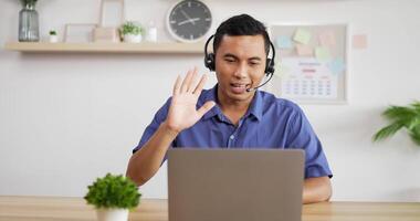 Portrait of Young Asian customer service support agent telemarketer wearing headset looking at laptop make business conference internet video call.