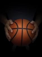 Basketball player holding a ball against black background photo