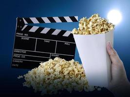 Hand with Popcorn, Movie clapperboard, on at blue background photo