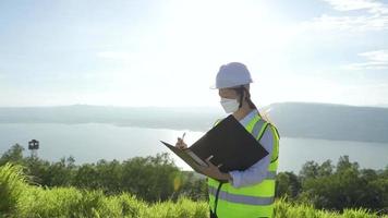 giovani ingegneri o tecnici con maschera e casco bianco stanno controllando il sistema della turbina eolica con un documento presso una fattoria di energia rinnovabile video