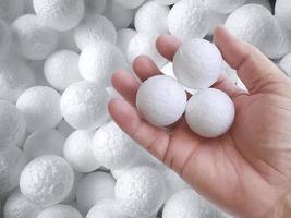 Hand holding white polystyrene foam beads ball drop from Styrofoam machine for fragile stuff packaging box on blue modern luxury background for decoration photo