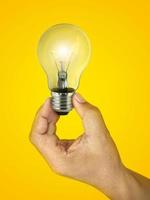 Concept creativity with Hand holding glowing light bulb  that shine glitter on yellow background photo