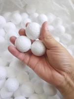 Hand holding white polystyrene foam beads ball drop from Styrofoam machine for fragile stuff packaging box on blue modern luxury background for decoration photo