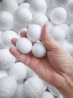 Hand holding white polystyrene foam beads ball drop from Styrofoam machine for fragile stuff packaging box on blue modern luxury background for decoration photo
