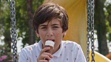 Teenager-Junge, der im Park auf Schaukel schwingt und Eis isst