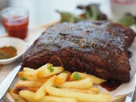 Pork Spareribs BBQ, Barbeque Pork Ribs with french fries vegetable salad, tomato sauce in a clear glass on wooden tray, food photo