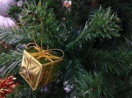 las decoraciones de los árboles verdes de navidad tienen una caja de regalo dorada, hojas en un fondo borroso foto