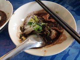 Thai Noodle, small noodles with pork stewed pork, meatball, pork liver and blood soup in white bowl, wooden chopsticks and spoon, Season the food with the seasoning, Thai food delicious photo