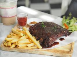 Pork Spareribs BBQ, Barbeque Pork Ribs with french fries vegetable salad, tomato sauce in a clear glass on wooden tray, food delicious photo
