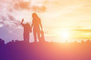 a silhouette of a happy young girl child the arms of his loving mother for a hug, in front of the sunset in the sky on a summer day. photo