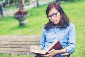 Hipster charming girl relaxing in the park while read book, Enjoy nature around. photo