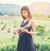 hermosa mujer sosteniendo una guitarra en su hombro, parque natural de verano afuera. foto