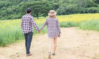 Young hipster couple relaxing in yellow flower field at summer. Enjoying with nature. photo