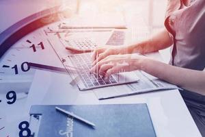 Mujer de oficina de negocios de mano de primer plano escribiendo en la superposición de computadora portátil con reloj de tiempo para el concepto de horas de trabajo foto