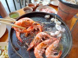 woman asia hand holding chopsticks grilled shrimp on a hot pan, on a wooden table photo