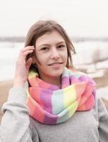 beautiful teenager girl wearing festive multicolored scarf and looking at camera. outdoors walking. happy girl with hair blowing with a wind photo