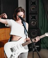 mujer joven tocando la guitarra eléctrica. Sala de ensayo de conciertos con altavoces. músico de rock femenino con guitarra blanca
