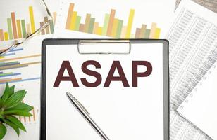 On a chart background magnifier, a pen and a sheet of paper with the text ASAP photo