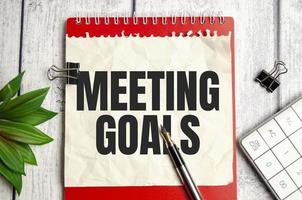 notebook over wood table background, focus on wooden blocks with letters making MEETING GOALS photo