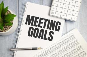 notebook over wood table background, focus on wooden blocks with letters making MEETING GOALS photo