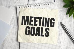 A notebook on wooden background with the text MEETING GOALS photo