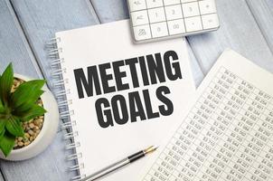 notebook over wood table background, focus on wooden blocks with letters making MEETING GOALS photo