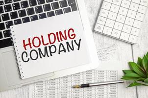 HOLDING COMPANY . text on white paper and laptop on wooden background photo