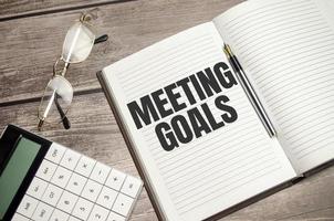 text MEETING GOALS on brown diary with calculator, glasses on wooden background photo