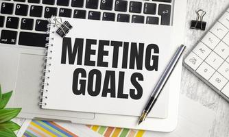 MEETING GOALS . text on white paper and laptop on wooden background photo
