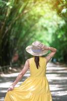Asian Woman in yellow dress and hat Traveling at green Bamboo Tunnel, Happy traveler walking Chulabhorn wanaram temple. landmark and popular for tourists attractions in Nakhon Nayok, Thailand photo