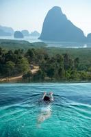 Happy woman in white swimsuit swimming in luxury pool hotel against Phang Nga bay background, Tourist relaxing at Samet Nang She, near Phuket in Southern Thailand. travel, trip and summer vacation photo