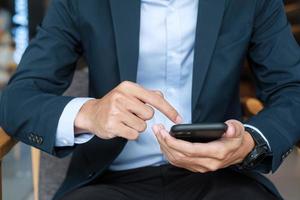 young Businessman in suit holding and using smartphone for sms messages, man typing touchscreen mobile phone in office or cafe. business, lifestyle, technology and Social media network concept photo