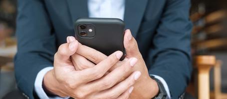 young Businessman in suit holding and using smartphone for sms messages, man typing touchscreen mobile phone in office or cafe. business, lifestyle, technology and Social media network concept photo