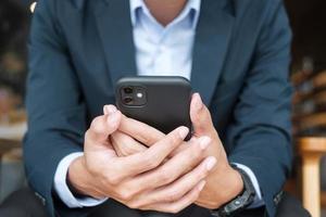 young Businessman in suit holding and using smartphone for sms messages, man typing touchscreen mobile phone in office or cafe. business, lifestyle, technology and Social media network concept photo