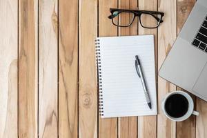 Top view Office desk with pen, computer laptop, blank notebook, plant pot and coffee cup on wood table background. workspace or home office with copy space for text concept photo