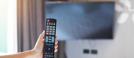 mano usando el control remoto para ajustar la televisión inteligente dentro de la habitación moderna en casa o en un hotel de lujo foto