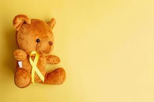 Yellow Ribbon with Bear doll on yellow color background for supporting kid living and illness. September Childhood Cancer Awareness month and World cancer day concept photo